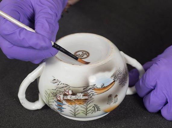 A pair of gloved hands applying a label to a ceramic pot.